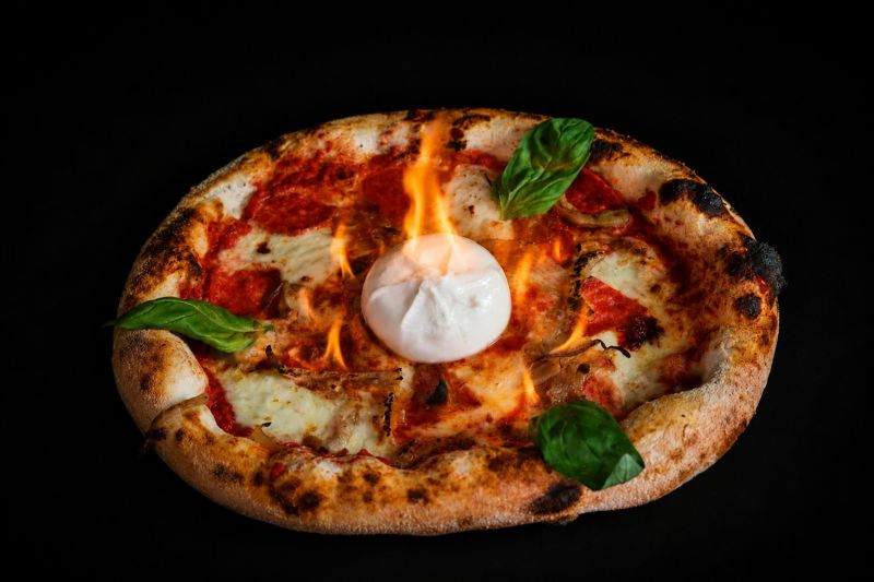 La pizza Flambé avvolta dalle fiamme, con la burratina al centro, salamino piccante e basilico