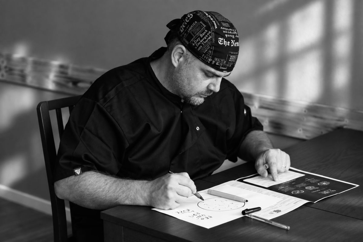 Fabrizio studia lo schema di una pizza su un foglio, seduto al tavolo
